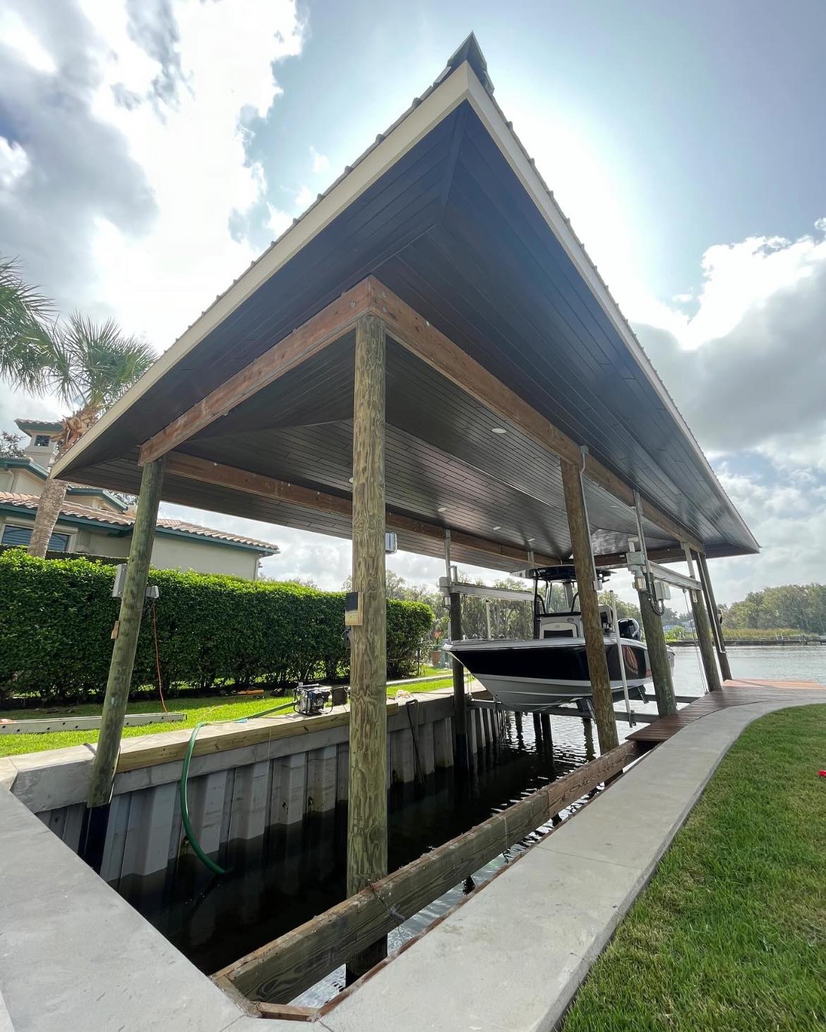 471226029_453834581098710_6495713644372997739_n - JSC Contracting Inc Wooden boat dock with a pitched metal roof, a motorboat in the slip, and a canal in the background.
