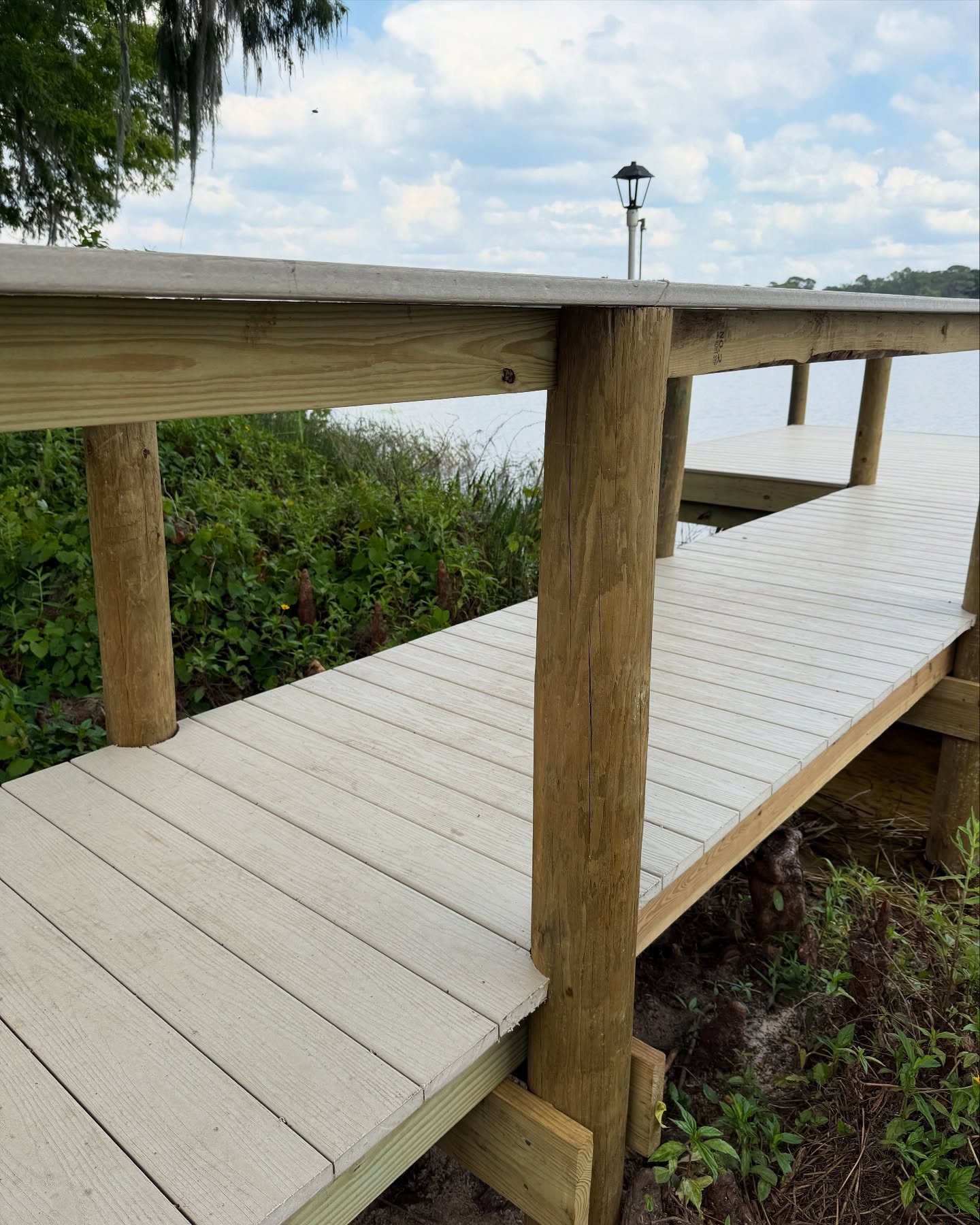495207803_17927680224049257_5282324596160732173_n - JSC Contracting Inc Wooden dock or boardwalk by the water with railing posts and a cloudy blue sky in the background