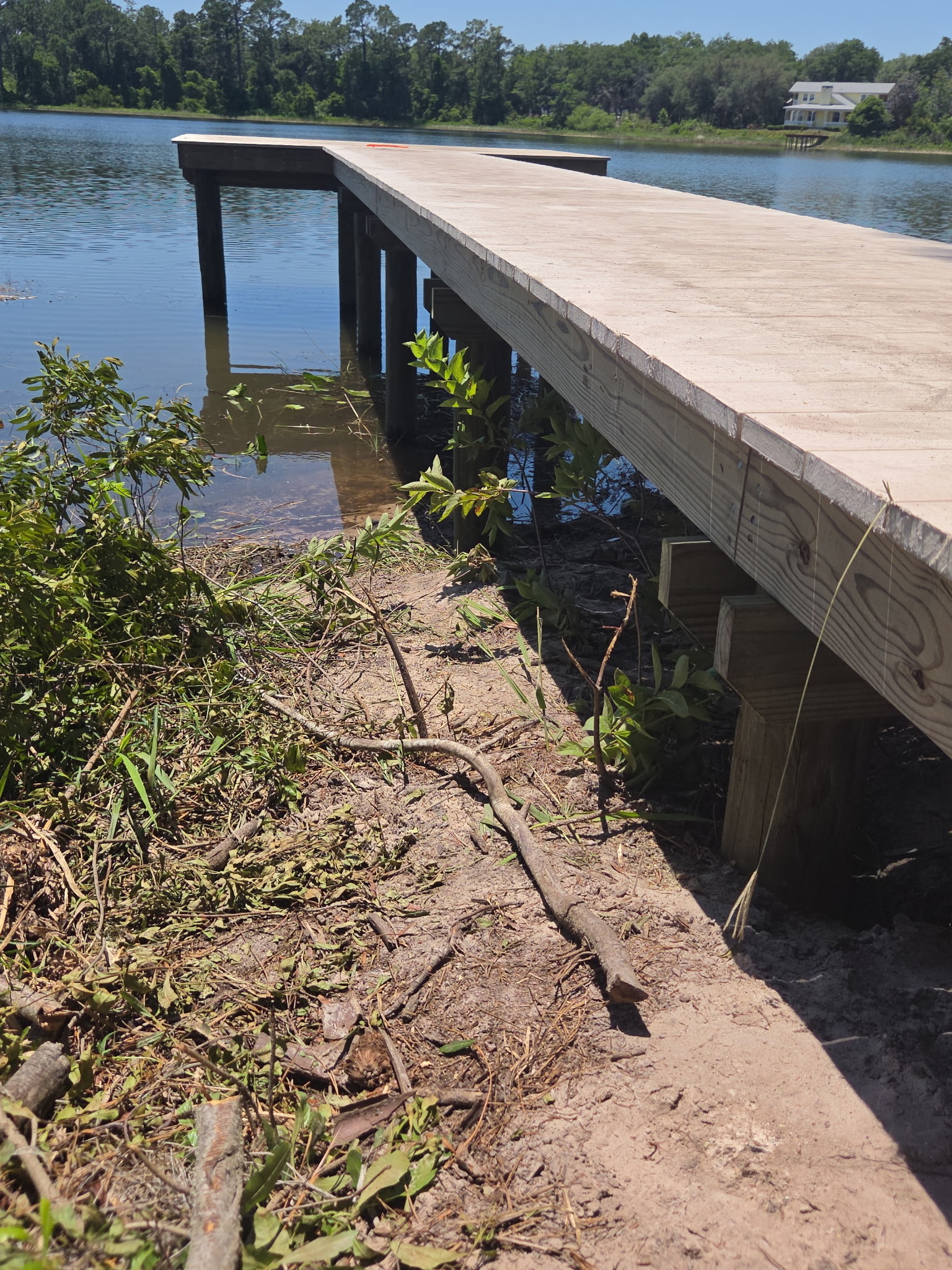 5670858573702878348 - JSC Contracting Inc Wooden dock extending into a calm lake with a forested shore and a distant white house.