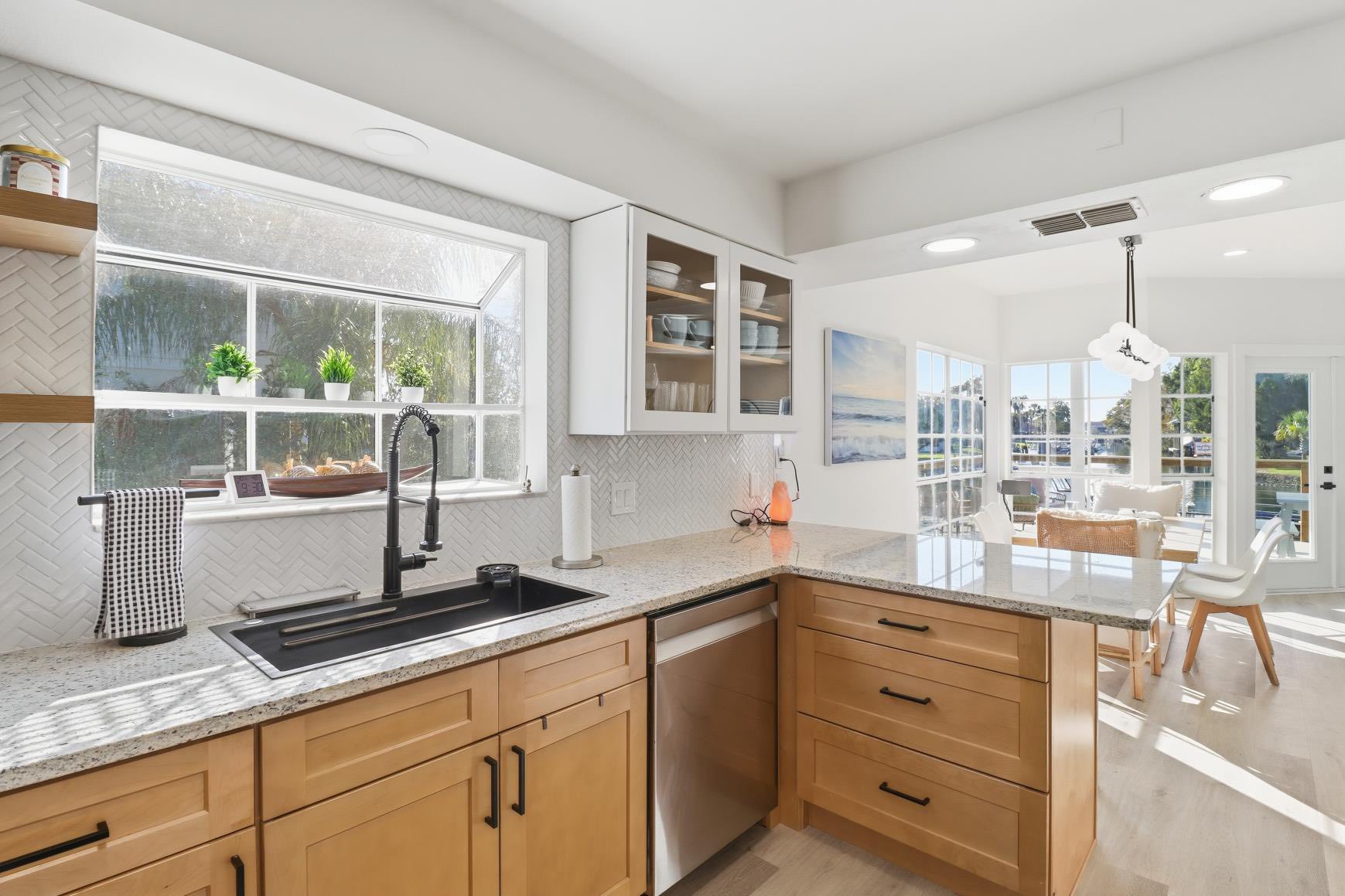 Bright, open kitchen with warm wood cabinets, speckled countertops, and a black pull-down faucet beside a large window.